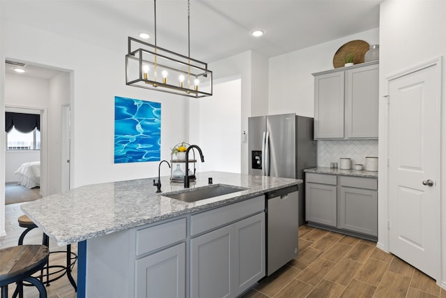 kitchen featuring wood tiled floor, stainless steel appliances, a sink, and gray cabinetry