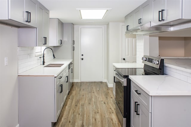 kitchen featuring gray cabinetry, backsplash, stainless steel electric range oven, sink, and light wood-type flooring