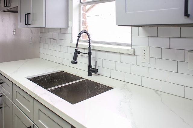 kitchen featuring sink, tasteful backsplash, gray cabinetry, and light stone countertops