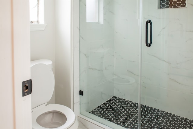 bathroom featuring a shower with door and toilet