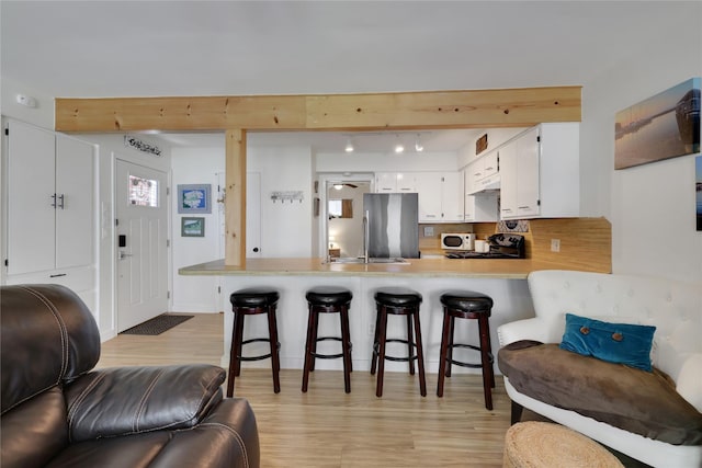 kitchen featuring a kitchen bar, light wood-type flooring, stainless steel refrigerator, kitchen peninsula, and white cabinets