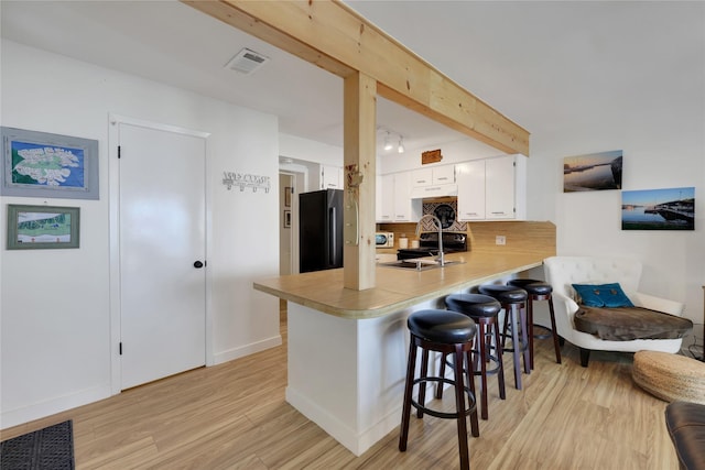 kitchen featuring sink, a breakfast bar area, high end black refrigerator, kitchen peninsula, and white cabinets