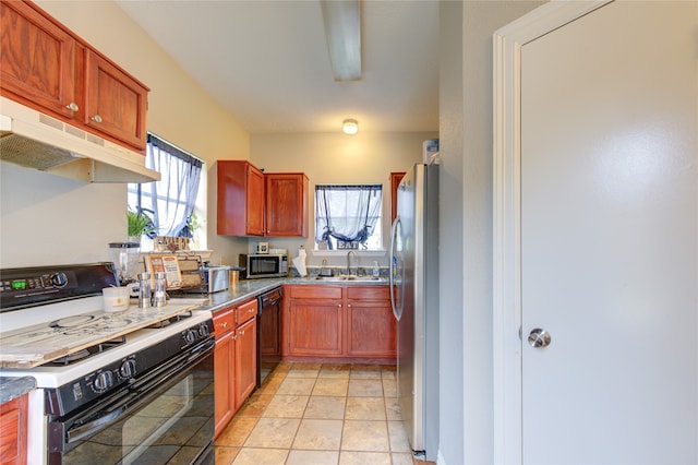 kitchen with appliances with stainless steel finishes, sink, light tile floors, and dark stone countertops