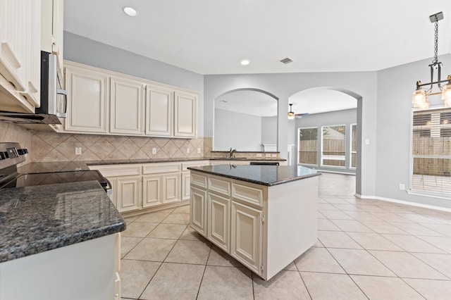 kitchen featuring cream cabinets, a center island, electric stove, sink, and backsplash