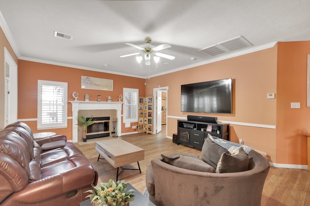 living room with visible vents, crown molding, light wood-style flooring, and a tiled fireplace