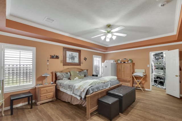 bedroom with ornamental molding, light wood-type flooring, a raised ceiling, and visible vents