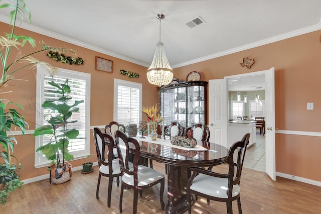 dining room featuring baseboards, visible vents, light wood-style flooring, and crown molding