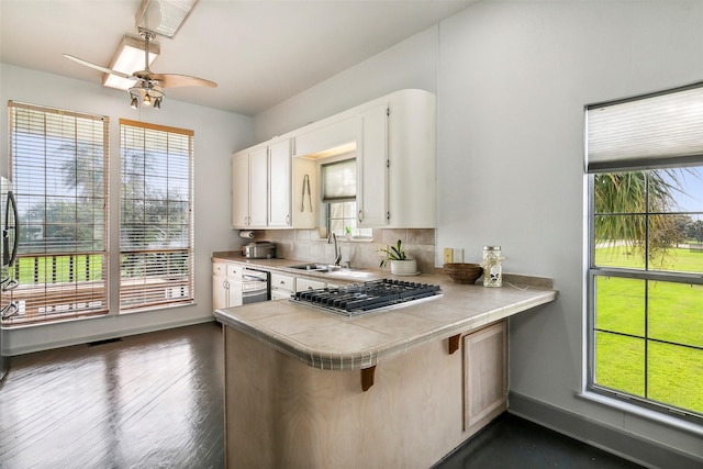 kitchen featuring a peninsula, a sink, white cabinetry, appliances with stainless steel finishes, and tasteful backsplash