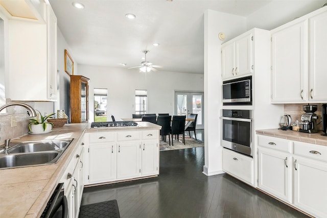 kitchen featuring dark wood-type flooring, a peninsula, stainless steel appliances, white cabinetry, and a sink