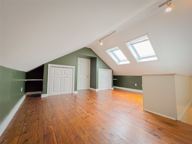 additional living space featuring hardwood / wood-style floors and vaulted ceiling with skylight