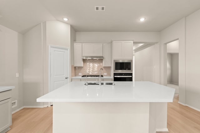 kitchen featuring an island with sink, sink, backsplash, white cabinetry, and light hardwood / wood-style floors