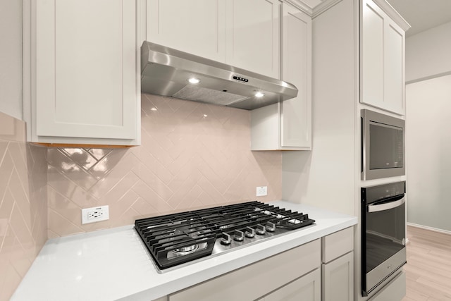 kitchen with white cabinets, backsplash, ventilation hood, appliances with stainless steel finishes, and light hardwood / wood-style floors