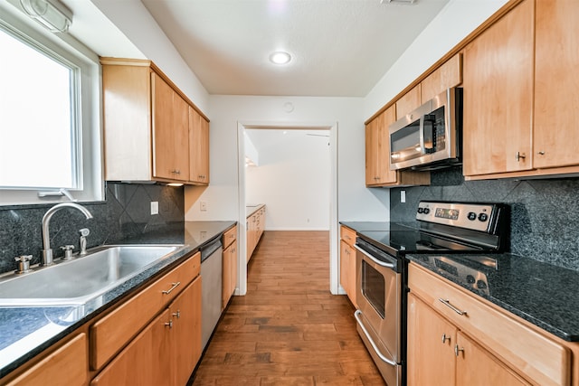 kitchen with appliances with stainless steel finishes, dark hardwood / wood-style flooring, tasteful backsplash, sink, and dark stone countertops