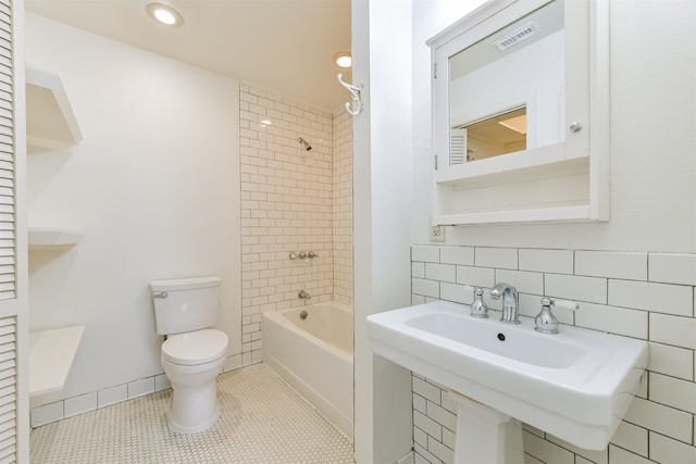 bathroom featuring tile patterned flooring, toilet, tiled shower / bath, and tile walls