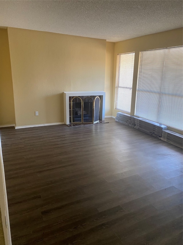 unfurnished living room featuring a tiled fireplace, a textured ceiling, and dark wood-type flooring