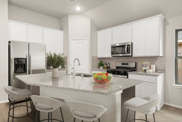 kitchen with stainless steel appliances, sink, a kitchen island with sink, white cabinets, and vaulted ceiling