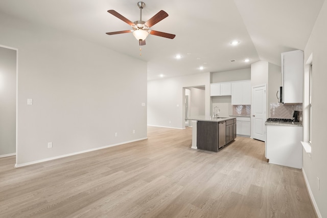 kitchen with white cabinets, sink, tasteful backsplash, a kitchen island with sink, and light wood-type flooring