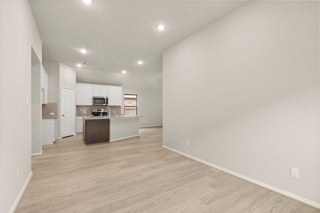 kitchen featuring white cabinets, light hardwood / wood-style floors, backsplash, and an island with sink