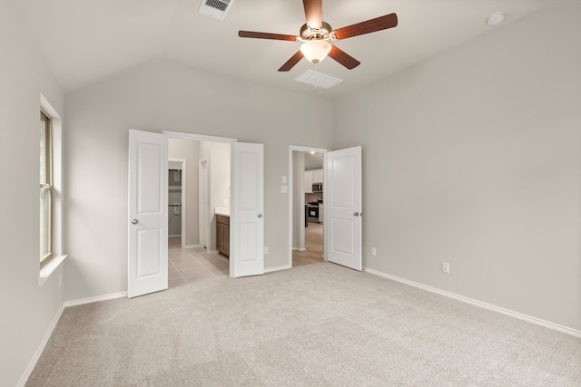 unfurnished bedroom with ceiling fan, connected bathroom, light colored carpet, multiple windows, and vaulted ceiling