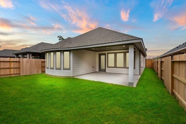 back house at dusk featuring a patio and a lawn