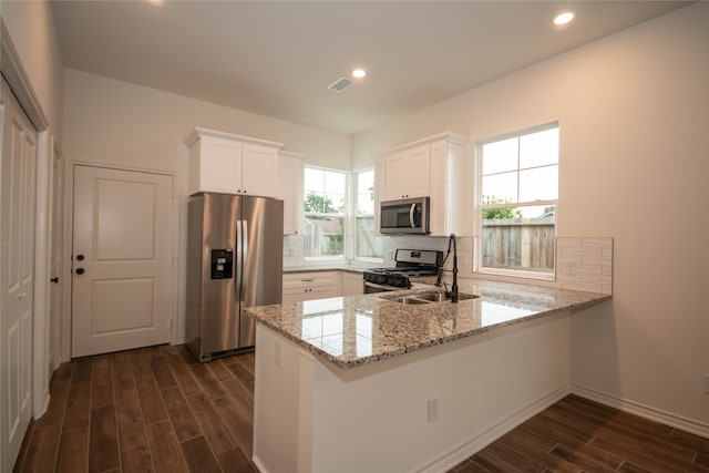 kitchen with kitchen peninsula, tasteful backsplash, white cabinetry, light stone countertops, and appliances with stainless steel finishes