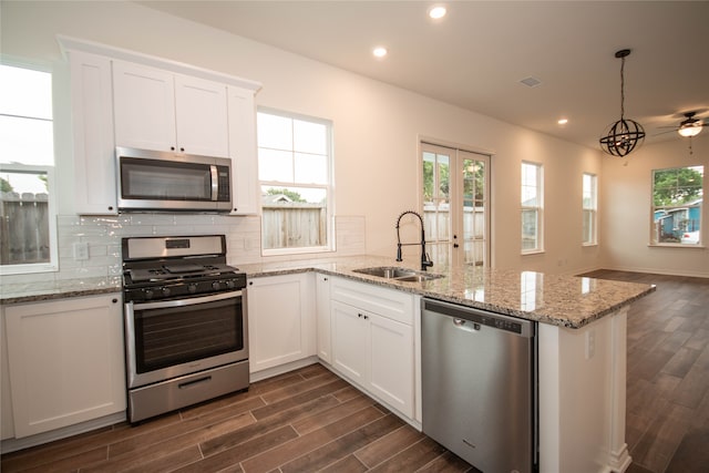 kitchen featuring kitchen peninsula, tasteful backsplash, decorative light fixtures, sink, and appliances with stainless steel finishes