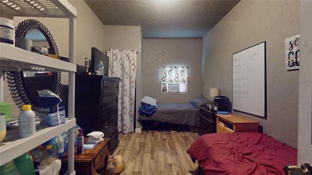 bedroom with light hardwood / wood-style floors, a textured ceiling, and cooling unit