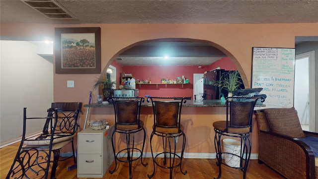 kitchen featuring a textured ceiling, kitchen peninsula, wood-type flooring, and a breakfast bar