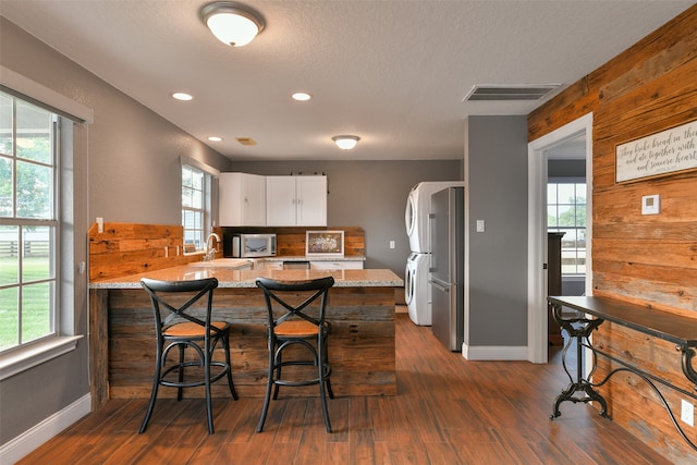 kitchen with white cabinetry, dark wood-type flooring, stacked washer and dryer, and light stone counters