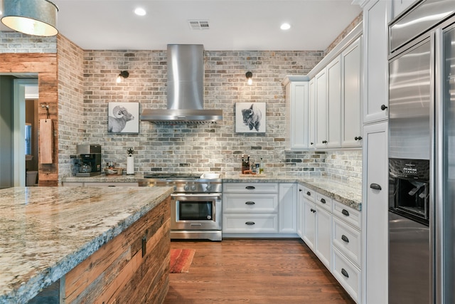 kitchen featuring wall chimney range hood, hardwood / wood-style floors, light stone countertops, white cabinets, and high quality appliances