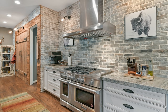 kitchen featuring double oven range, brick wall, and wall chimney exhaust hood