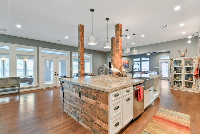 kitchen featuring french doors, stainless steel dishwasher, a center island with sink, decorative light fixtures, and dark wood-type flooring