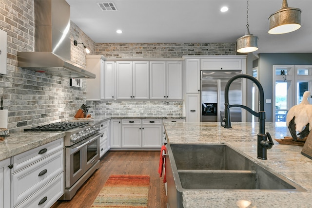 kitchen with pendant lighting, dark hardwood / wood-style flooring, high quality appliances, wall chimney exhaust hood, and sink