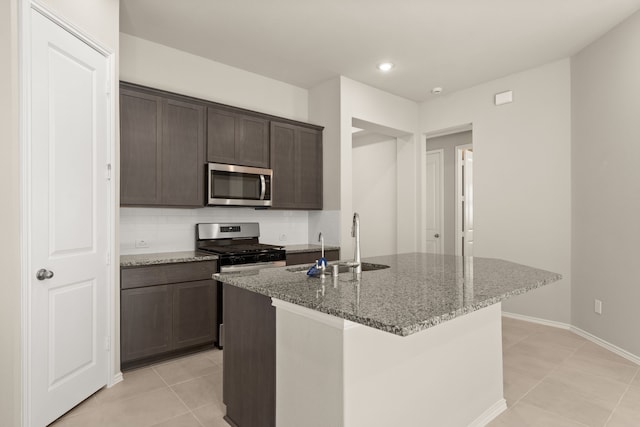 kitchen featuring appliances with stainless steel finishes, light stone counters, dark brown cabinetry, and a kitchen island with sink