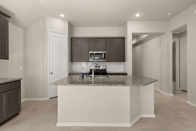 kitchen with dark brown cabinets, a center island with sink, sink, light stone counters, and stainless steel appliances