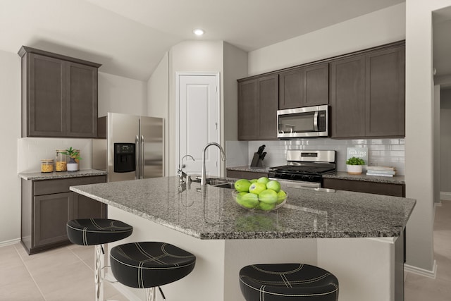 kitchen featuring dark stone counters, a kitchen island with sink, stainless steel appliances, and tasteful backsplash