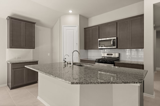 kitchen with an island with sink, stainless steel appliances, dark stone countertops, sink, and backsplash