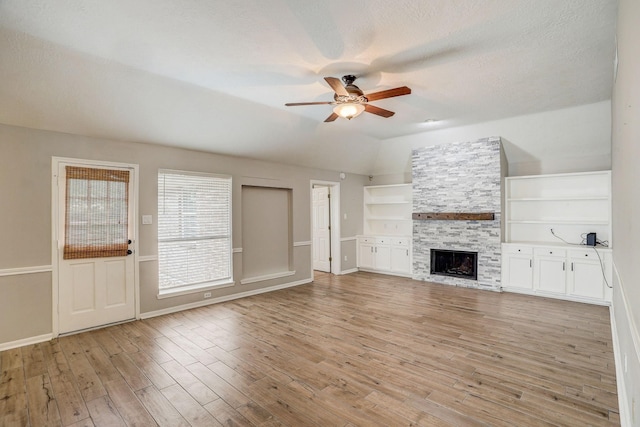 unfurnished living room featuring light wood-style flooring, a textured ceiling, a fireplace, lofted ceiling, and ceiling fan