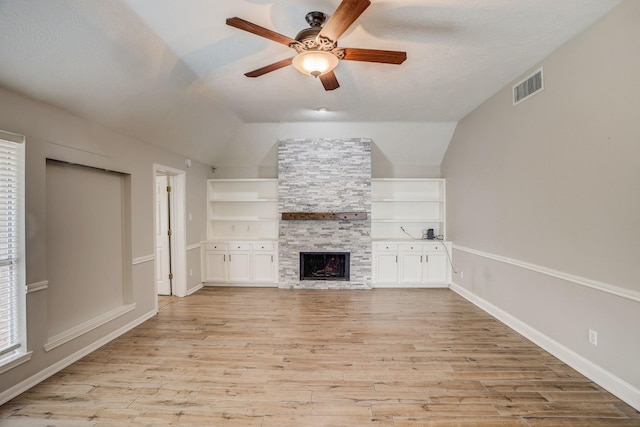 unfurnished living room featuring light wood-type flooring, visible vents, a textured ceiling, a stone fireplace, and vaulted ceiling