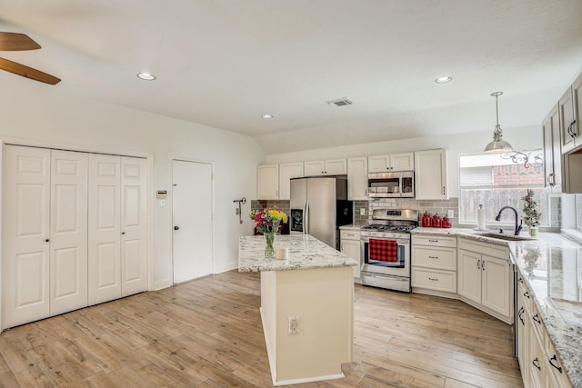 kitchen with a sink, stainless steel appliances, vaulted ceiling, light wood-type flooring, and backsplash