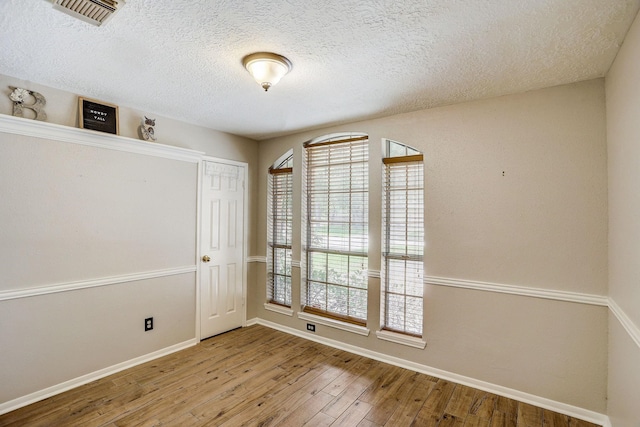 spare room featuring visible vents, a healthy amount of sunlight, baseboards, and wood-type flooring