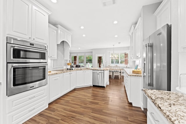 kitchen featuring light stone countertops, decorative light fixtures, stainless steel appliances, and white cabinetry