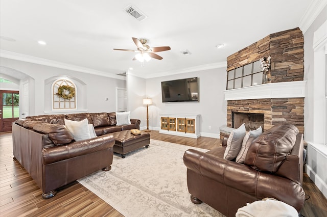 living room featuring hardwood / wood-style flooring, a stone fireplace, ceiling fan, and ornamental molding