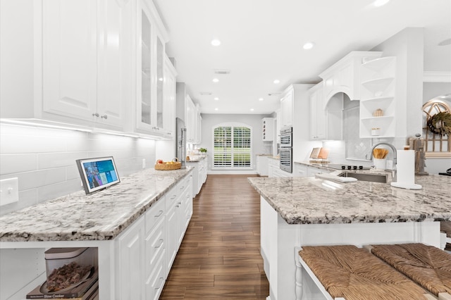 kitchen with white cabinets, backsplash, light stone countertops, and sink