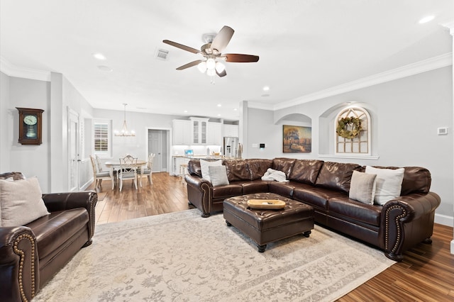 living room featuring hardwood / wood-style floors, ceiling fan with notable chandelier, and ornamental molding