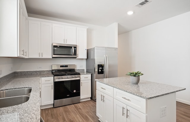 kitchen with stainless steel appliances, white cabinetry, hardwood / wood-style flooring, and light stone countertops