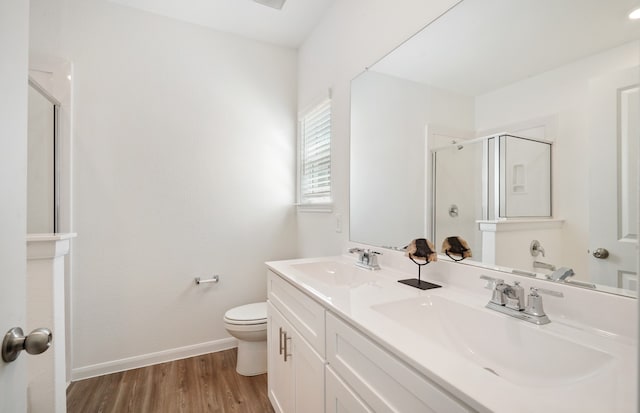 bathroom featuring hardwood / wood-style floors, double sink, vanity with extensive cabinet space, a shower with door, and toilet