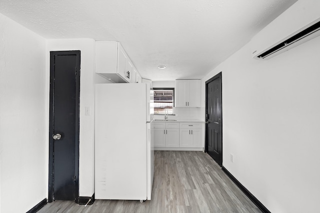 kitchen with light hardwood / wood-style flooring, white fridge, a wall mounted air conditioner, sink, and white cabinetry