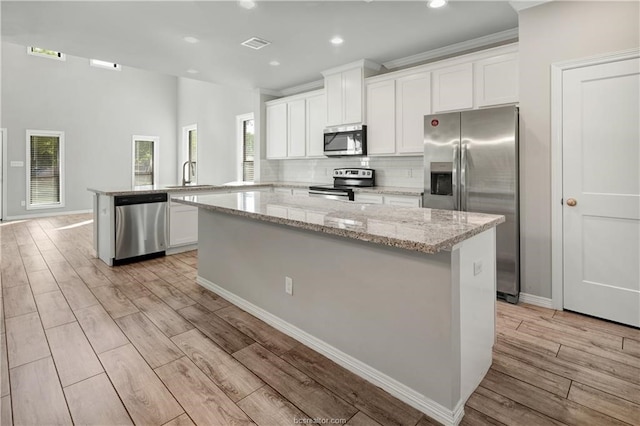 kitchen featuring a center island, light wood-type flooring, backsplash, and appliances with stainless steel finishes