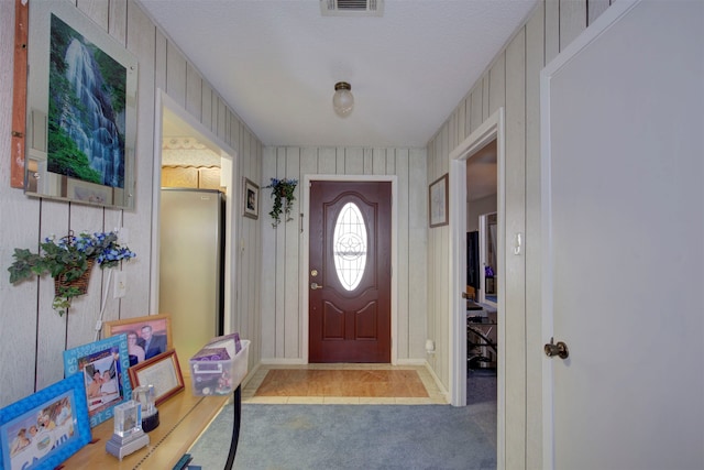 foyer entrance with a textured ceiling, carpet flooring, and wood walls